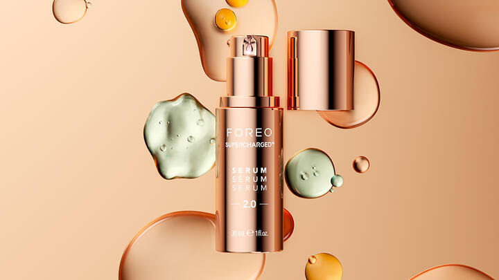 FOREO SUPERCHARGED Serum floating in a light brown space, drops of cosmetic liquid behind it